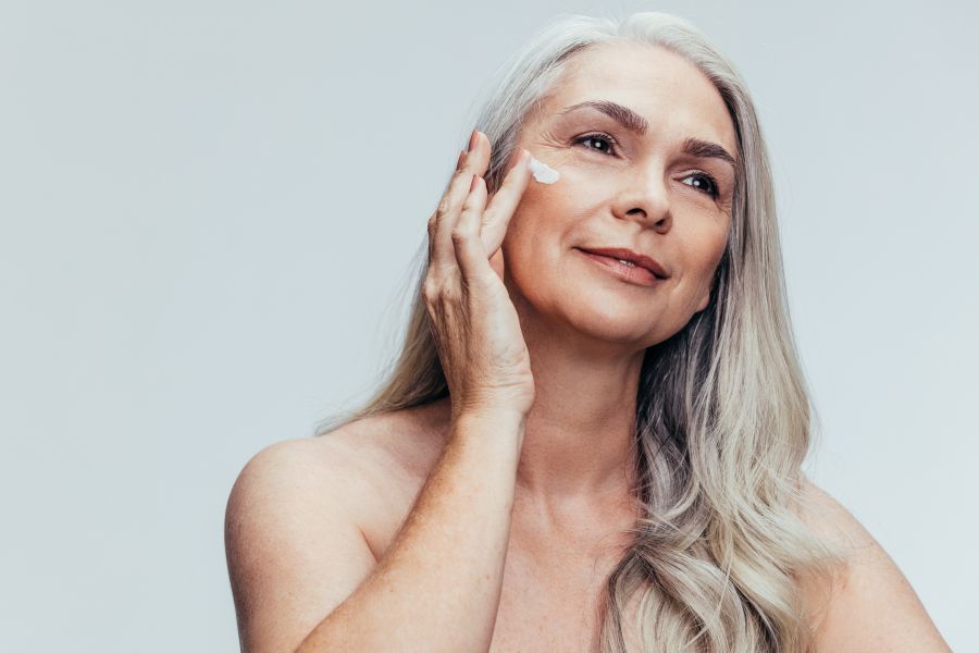 An older woman putting lotion on her cheek.