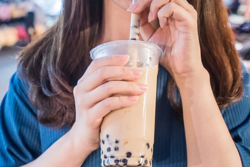 A person holding a plastic straw and drinking bubble tea from a plastic cup