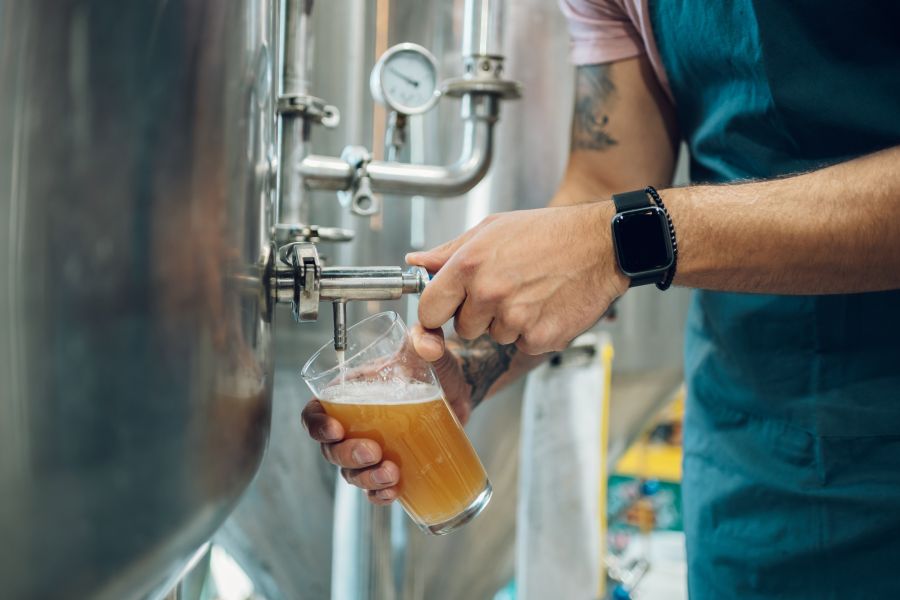 man pours beer into glass from brewery tank
