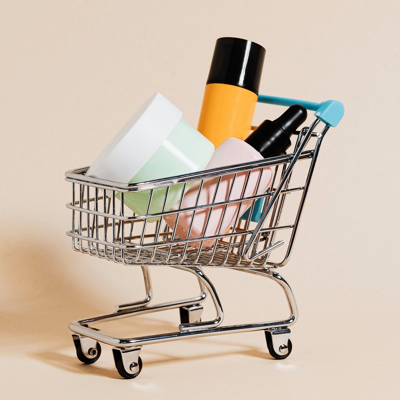 A miniature shopping cart filled with unbranded cosmetics products.