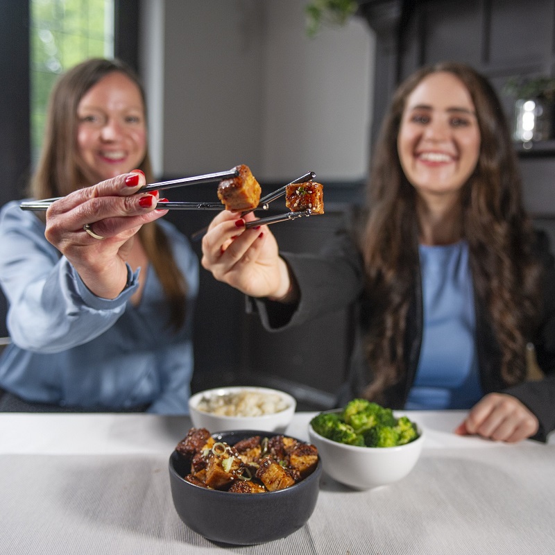 two women holding cell-based meat on sticks.