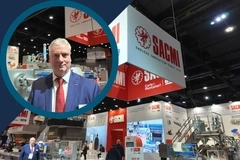 SACMI exhibition stand showcasing industrial packaging machinery, with a man in a blue suit and red tie featured in a circular inset. SACMI exhibition stand showcasing industrial packaging machinery, with a man in a blue suit and red tie featured in a circular inset.