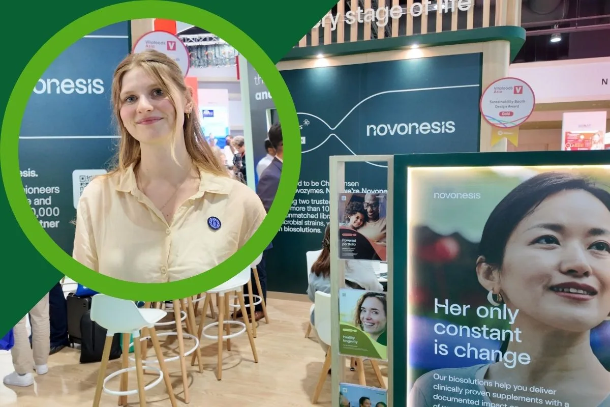 Image Vitafoods Asia 2026 Novonesis video thumbnail: Woman standing at the Novonesis exhibition booth, surrounded by branded displays promoting biosolutions and sustainability