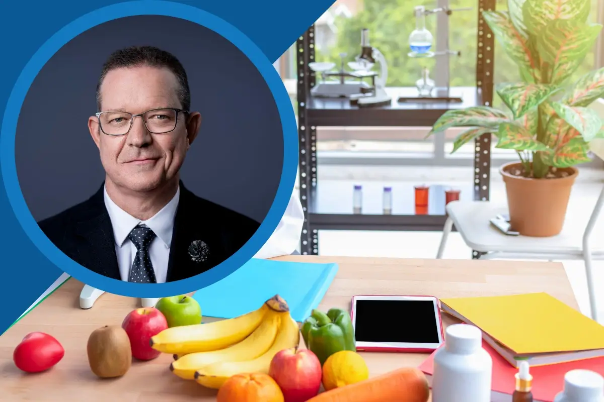 Portrait of a suited man beside a bright nutrition lab scene with fresh fruit, vegetables, supplements, and scientific equipment.